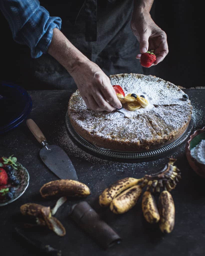 hands topping cake with fruit