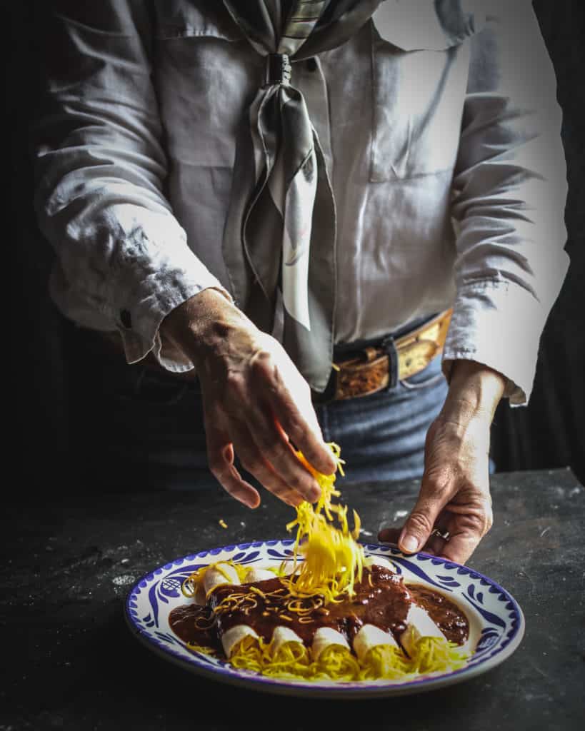 hands putting cheese on enchiladas