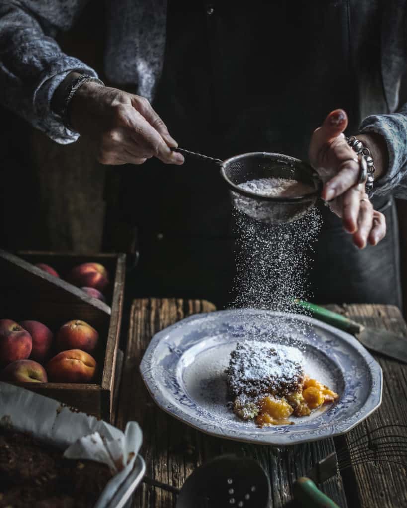 hands sprinkling sugar on cake