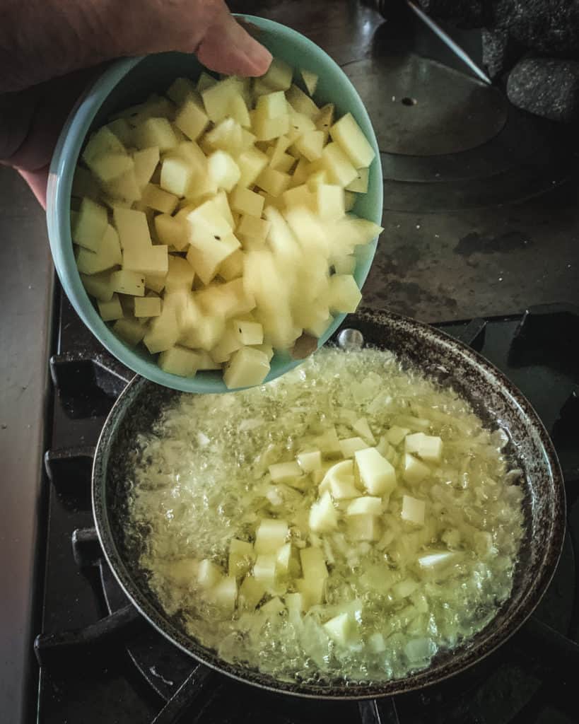 adding potatoes to frying pan