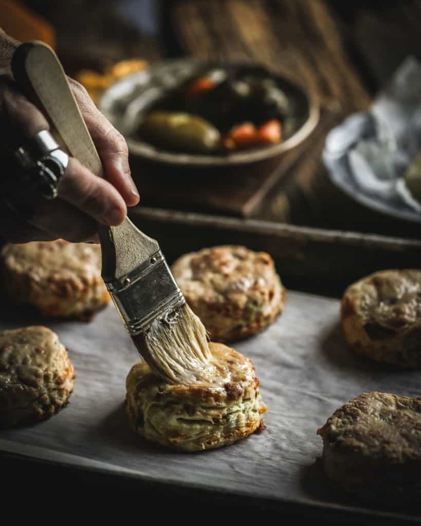 hand brushing butter on biscuit