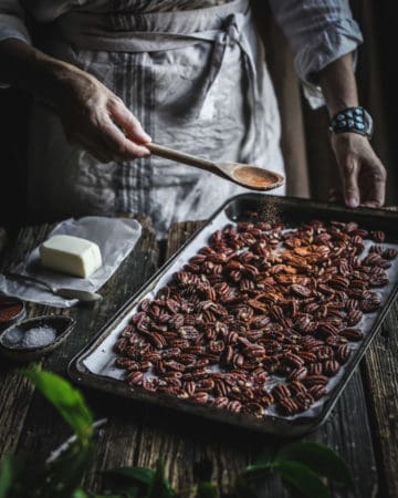 woman seasoning pan of roasted pecans