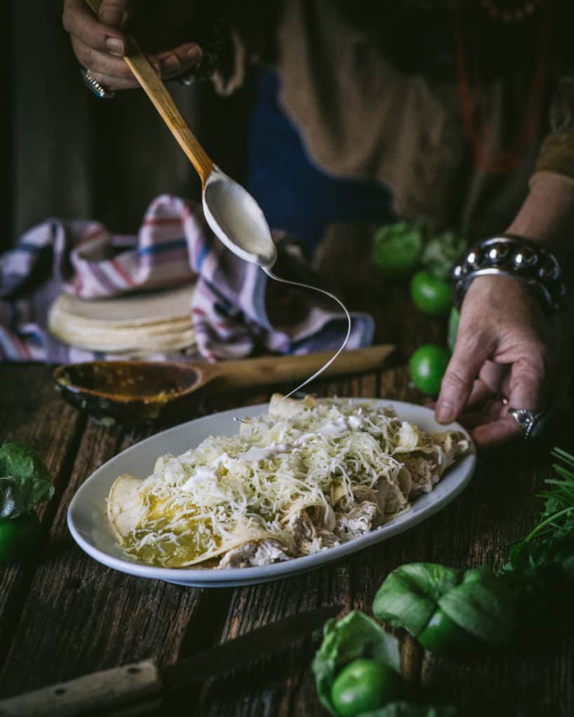 spoon swirling cream over enchiladas