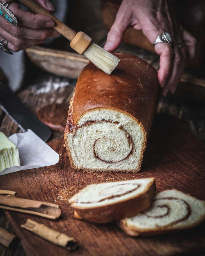 hand brushing butter on cinnamon swirl bread