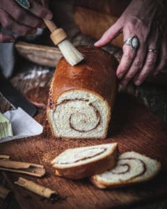 hand brushing butter on cinnamon swirl bread