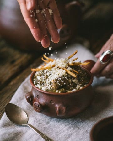 hand sprinkling cheese on bowl of chili verde