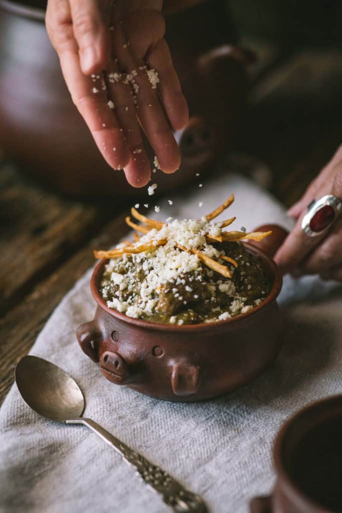 hand sprinkling cheese on bowl of chili verde