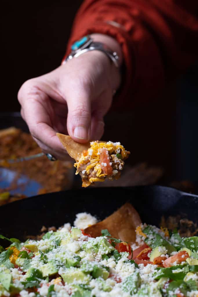 woman holding tortilla chip with 7 layer dip