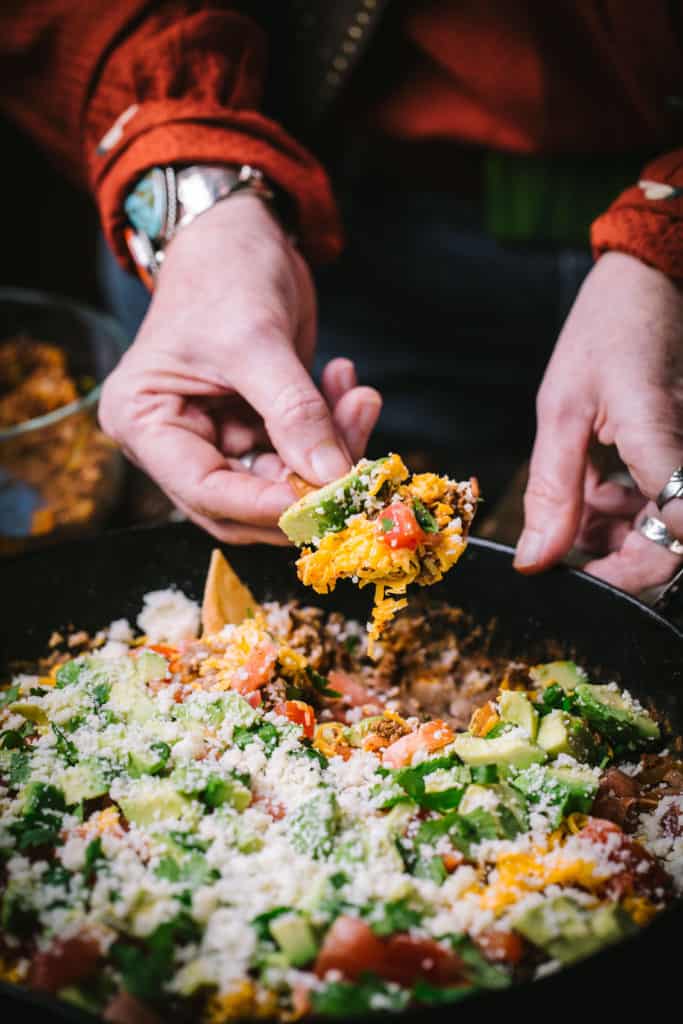 woman holding tortilla chip with 7 layer dip