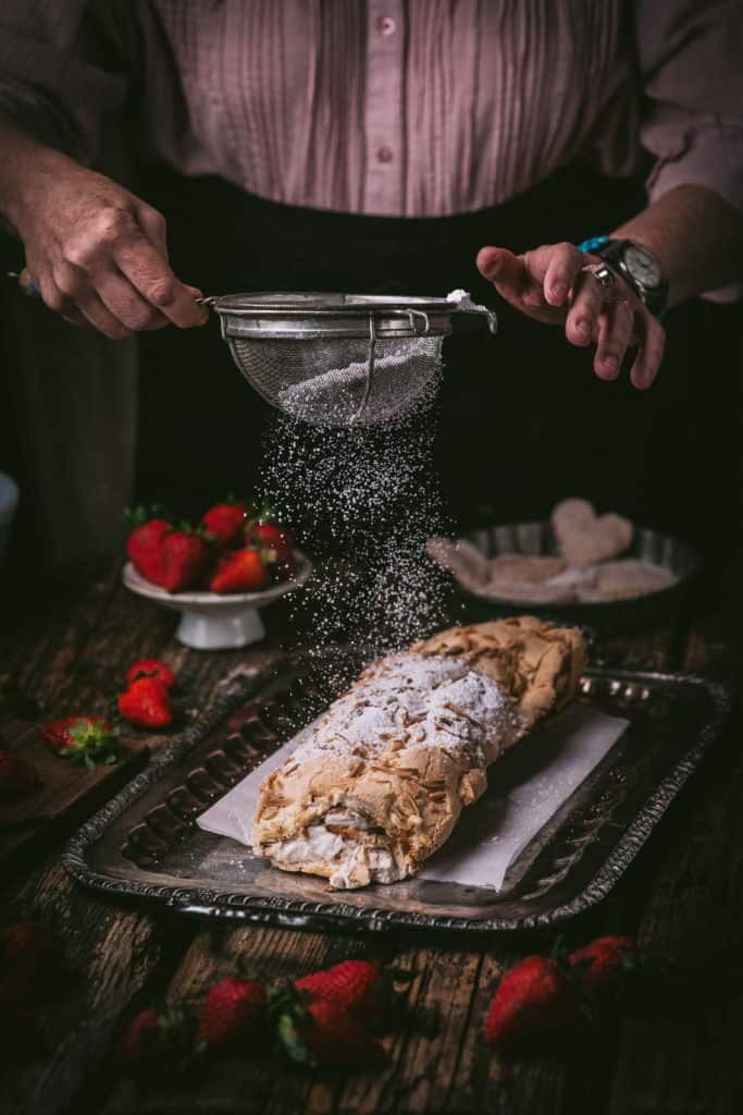 woman dusting strawberry meringue roll with powdered sugar