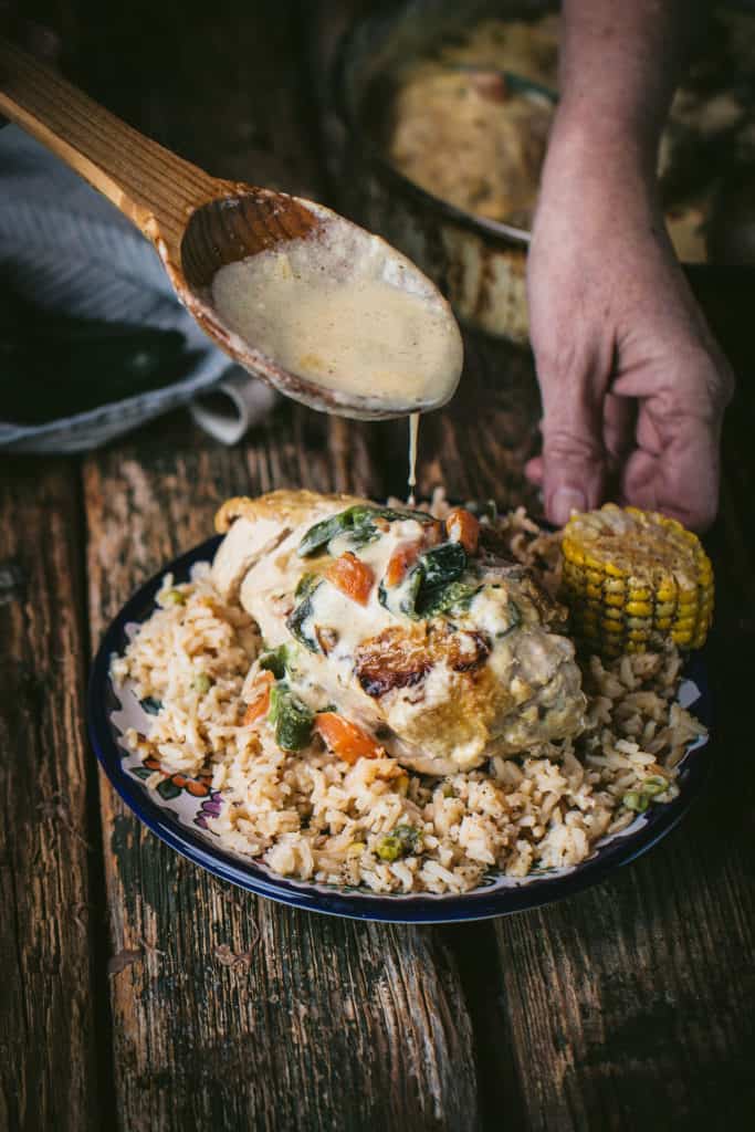 woman drizzling sauce on chicken on poblano cream sauce