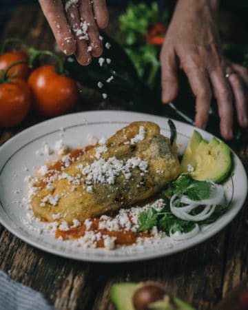 hand garnishing chiles rellenos with cheese