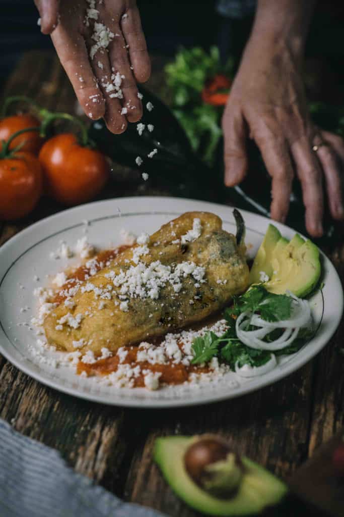 hand garnishing chiles rellenos with cheese