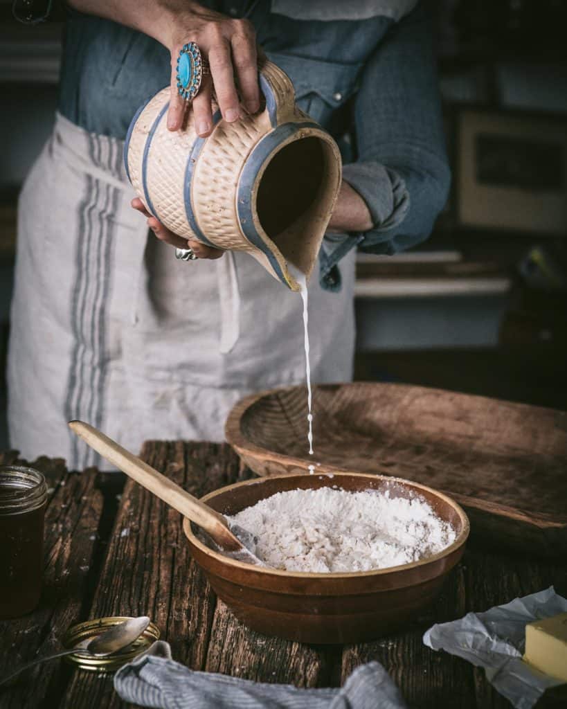woman pouring milk into bowl of flour