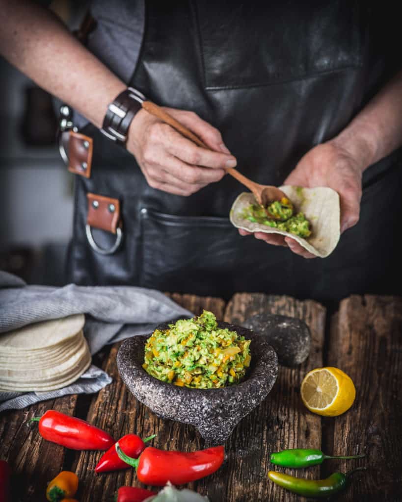 woman serving roasted vegetable avocado salsa with tortilla
