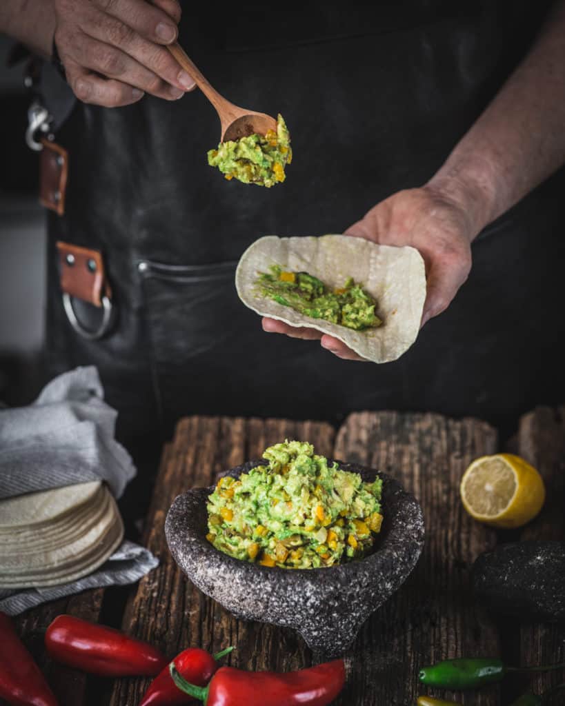 woman serving roasted vegetable avocado salsa with tortilla