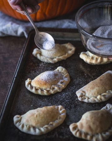 spoon sprinkling sugar on pumpkin empanada