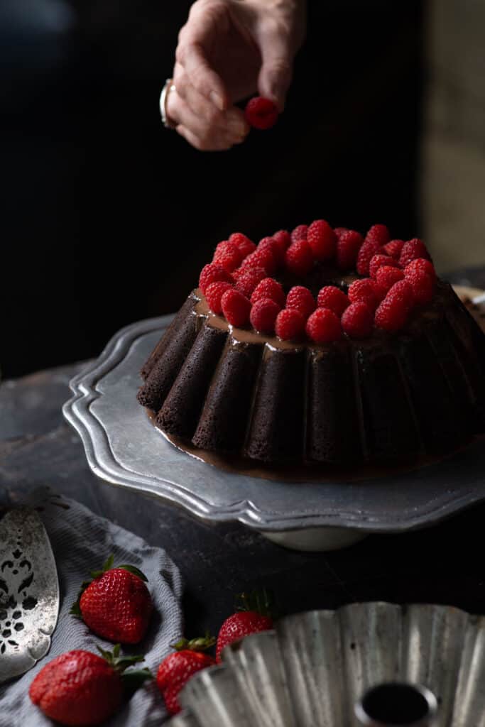 hand placing raspberry on cake
