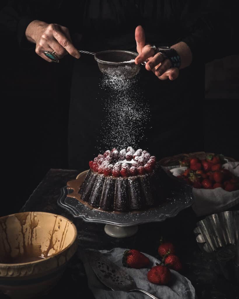 woman sprinkling sugar over Chocolate Tres Leches Cake