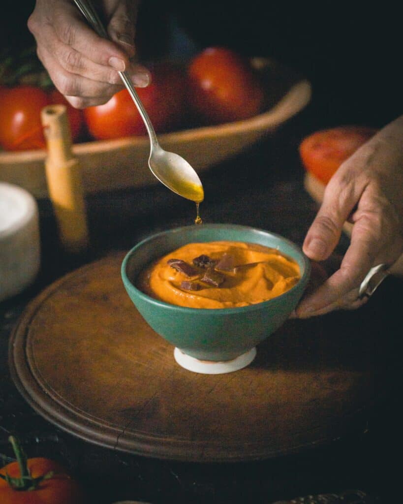 Olive oil dripping into a bowl of salmorejo