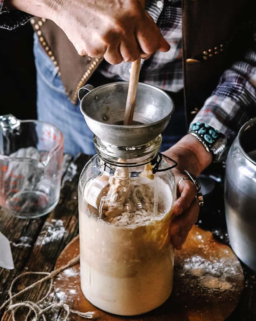 hands stirring sourdough starter in a jar