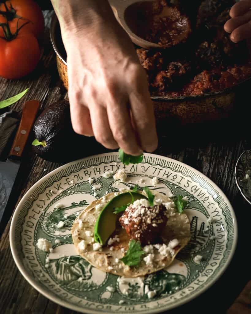 hand garnishing meatball taco with toppings