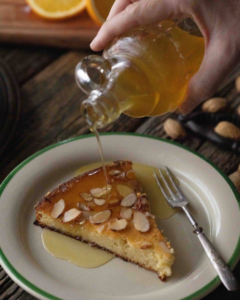 hand pouring orange syrup on cake