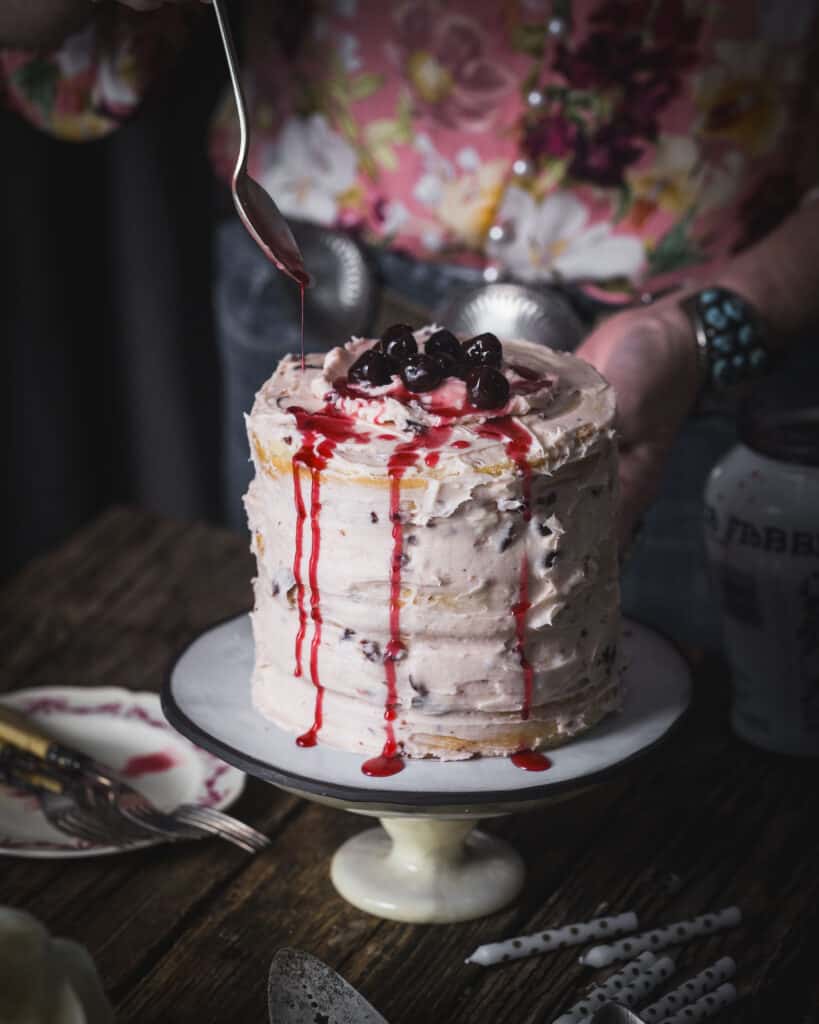 woman spooning cherries over Wild Cherry Cake on a table