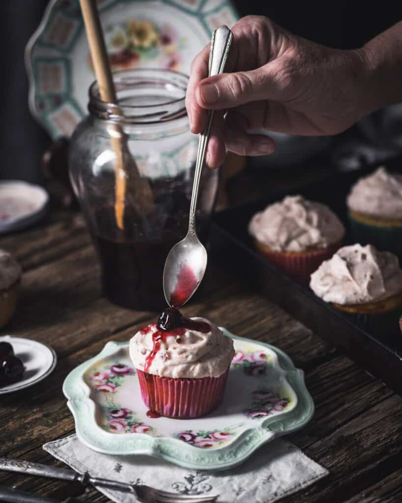 woman placing cherry on top of a cupcake with a spoon