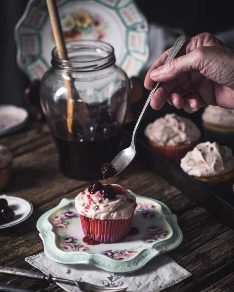 woman placing cherry on top of a cupcake with a spoon