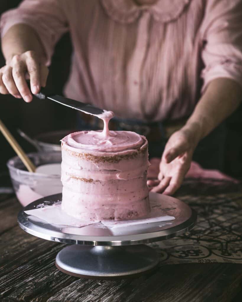 woman frosting Strawberry cake with Strawberry Cream Cheese Frosting